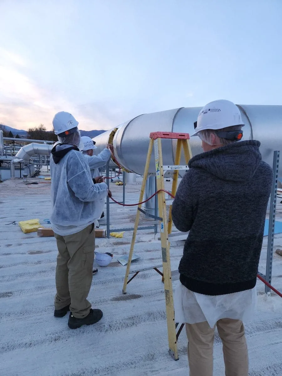 Three commercial air duct cleaners working on a rooftop air duct system