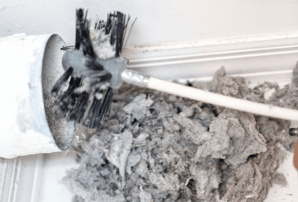 A picture of a dirty dryer vent, lint, and a brush.