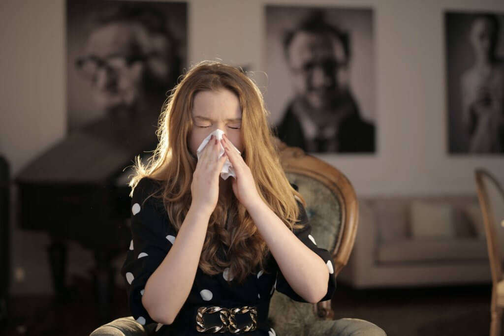 Woman with allergies sneezing and holding a tissue to her nose.